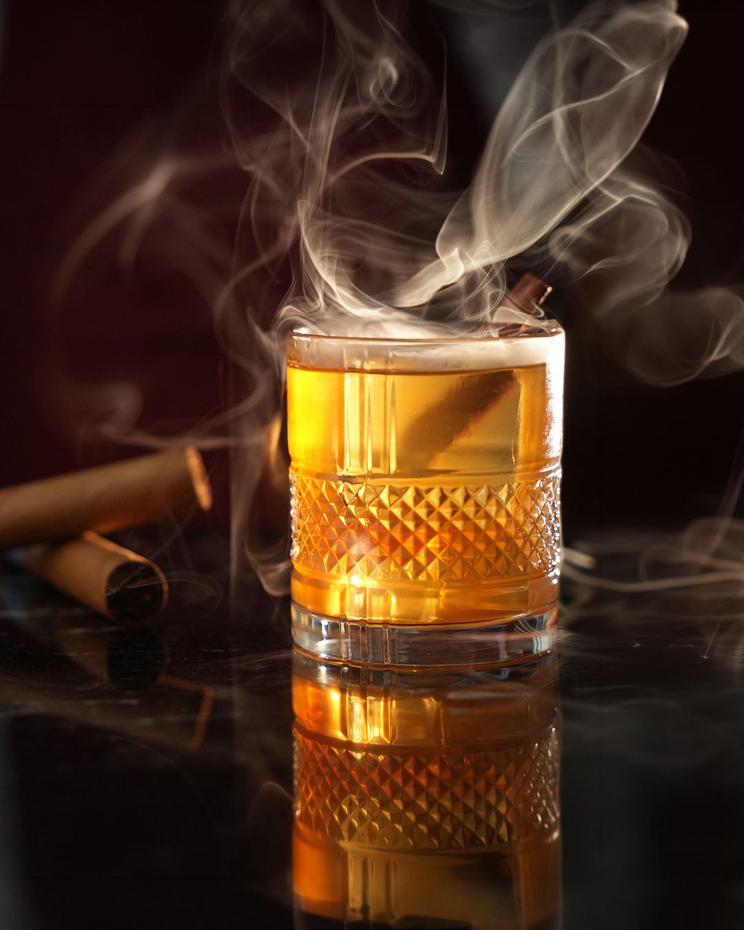 Smoke drifting from a cut-crystal rocks glass with an amber drink, cigars resting beside it