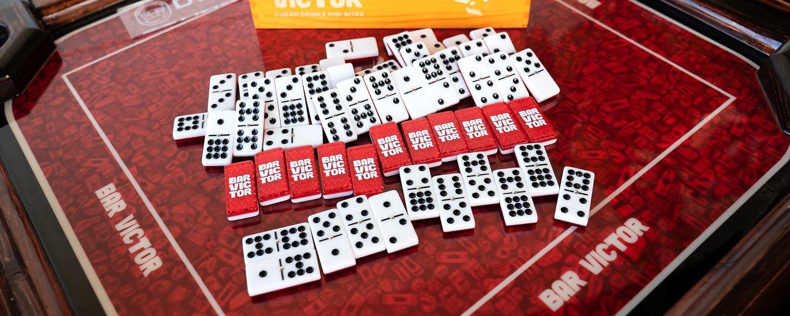Bar Victor branded dominoes spread across a red table
