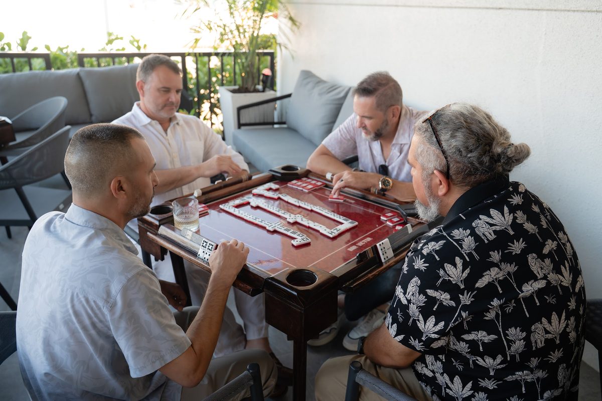 Four guests playing dominoes at a table on the Bar Victor patio