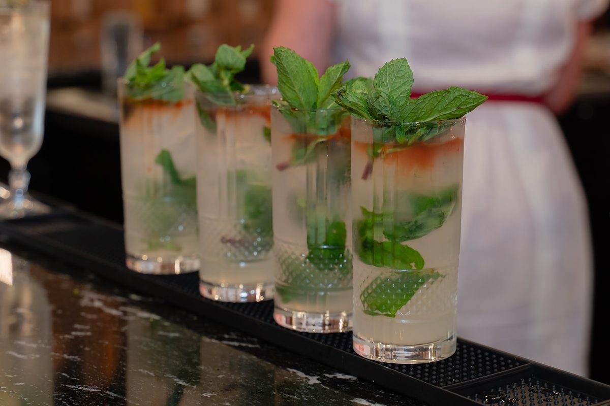 A row of mojitos with mint and lime lined up on the bar
