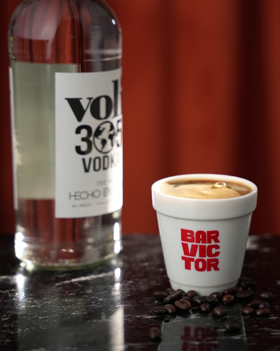 The Cafecito Martini served in a Bar Victor cup topped with coffee foam and espresso beans, beside a bottle of Voli 305 vodka