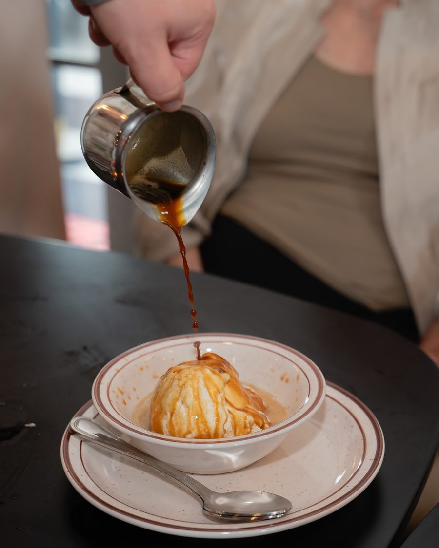 A dessert in a white bowl with a sauce being poured over it at the table