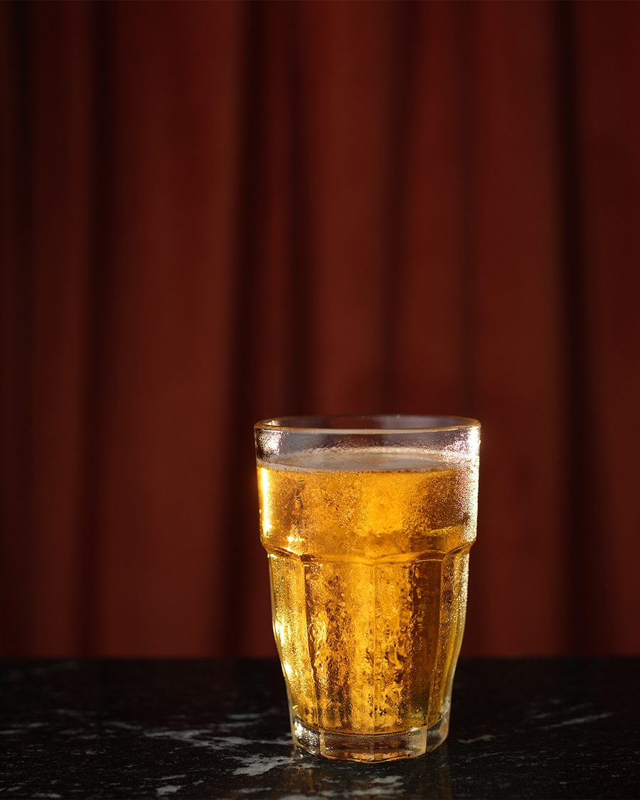 A cold draft beer in a tall glass against the red curtain