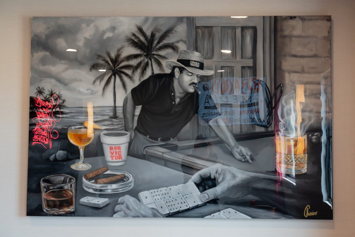 A black-and-white mural of a man rolling cigars at a table, with a Bar Victor cup painted in the corner