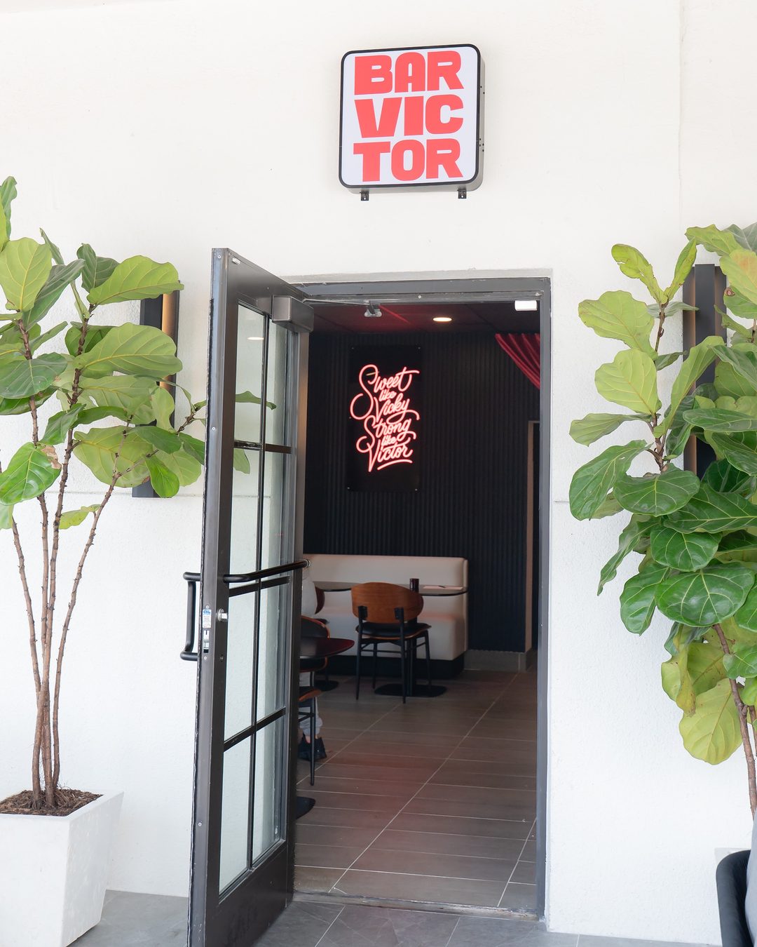 The entrance to Bar Victor with the red sign above the door and a neon sign glowing inside